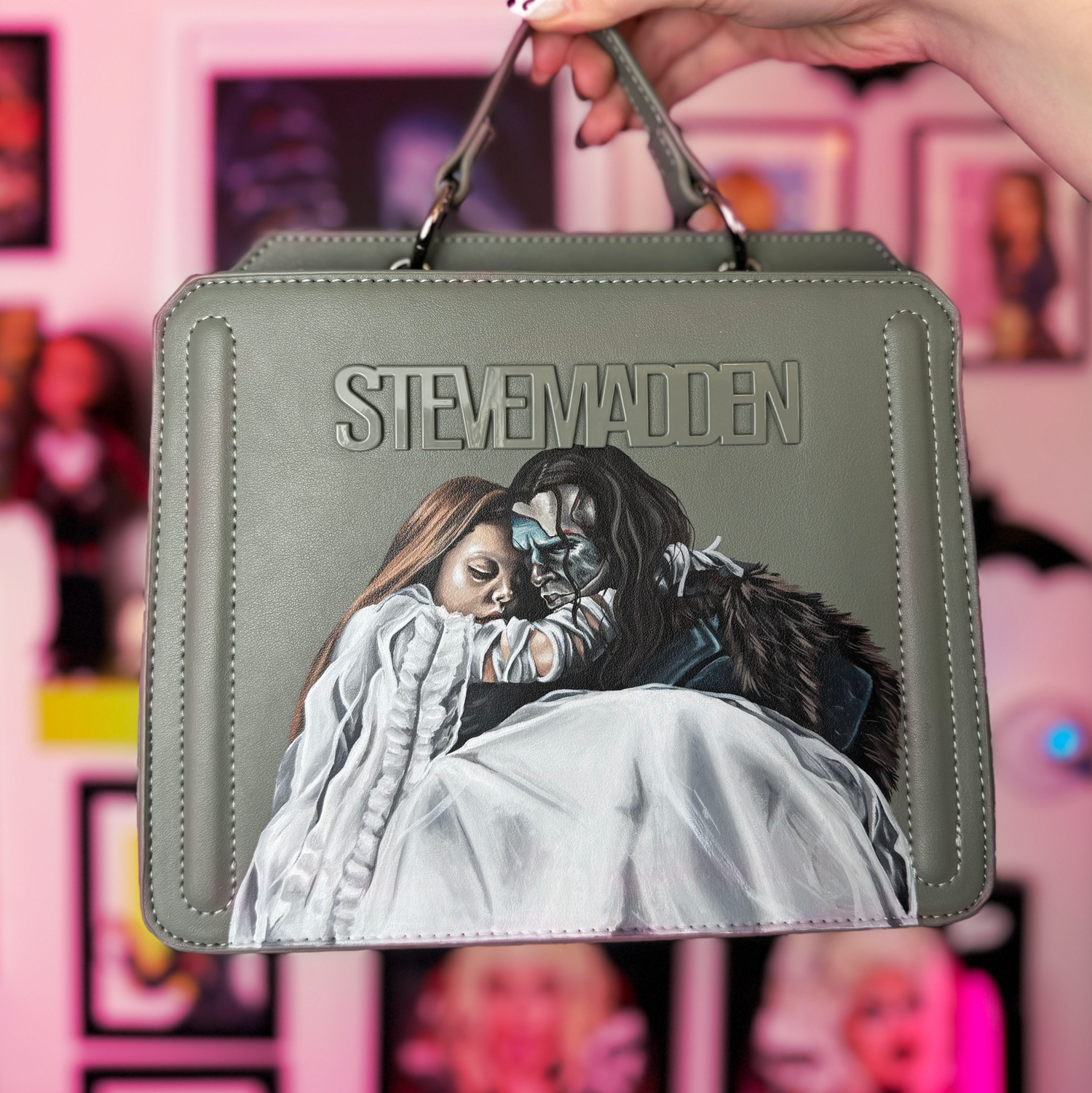 Gray handbag with a printed design and 'Steve Madden' branding, held against a colorful background.